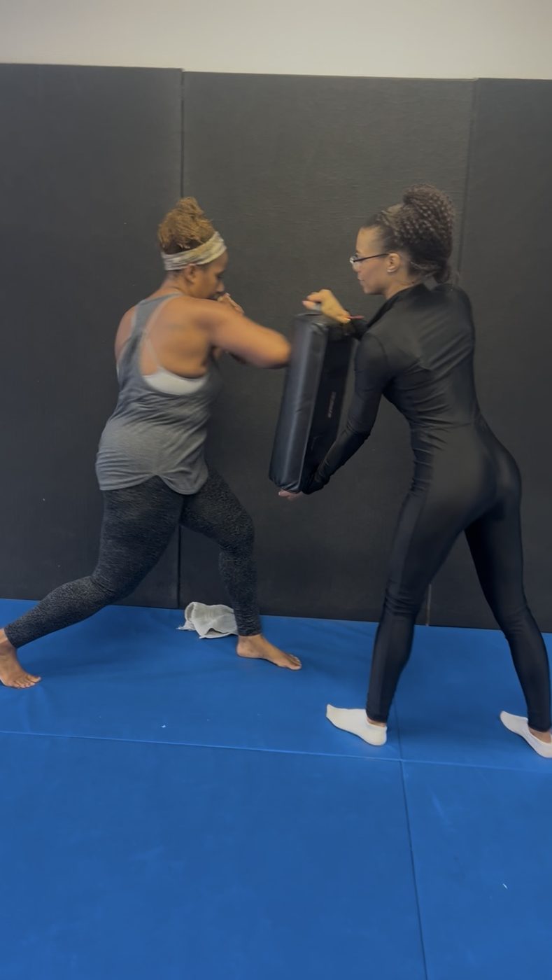 Women training together, one holding pads for the other